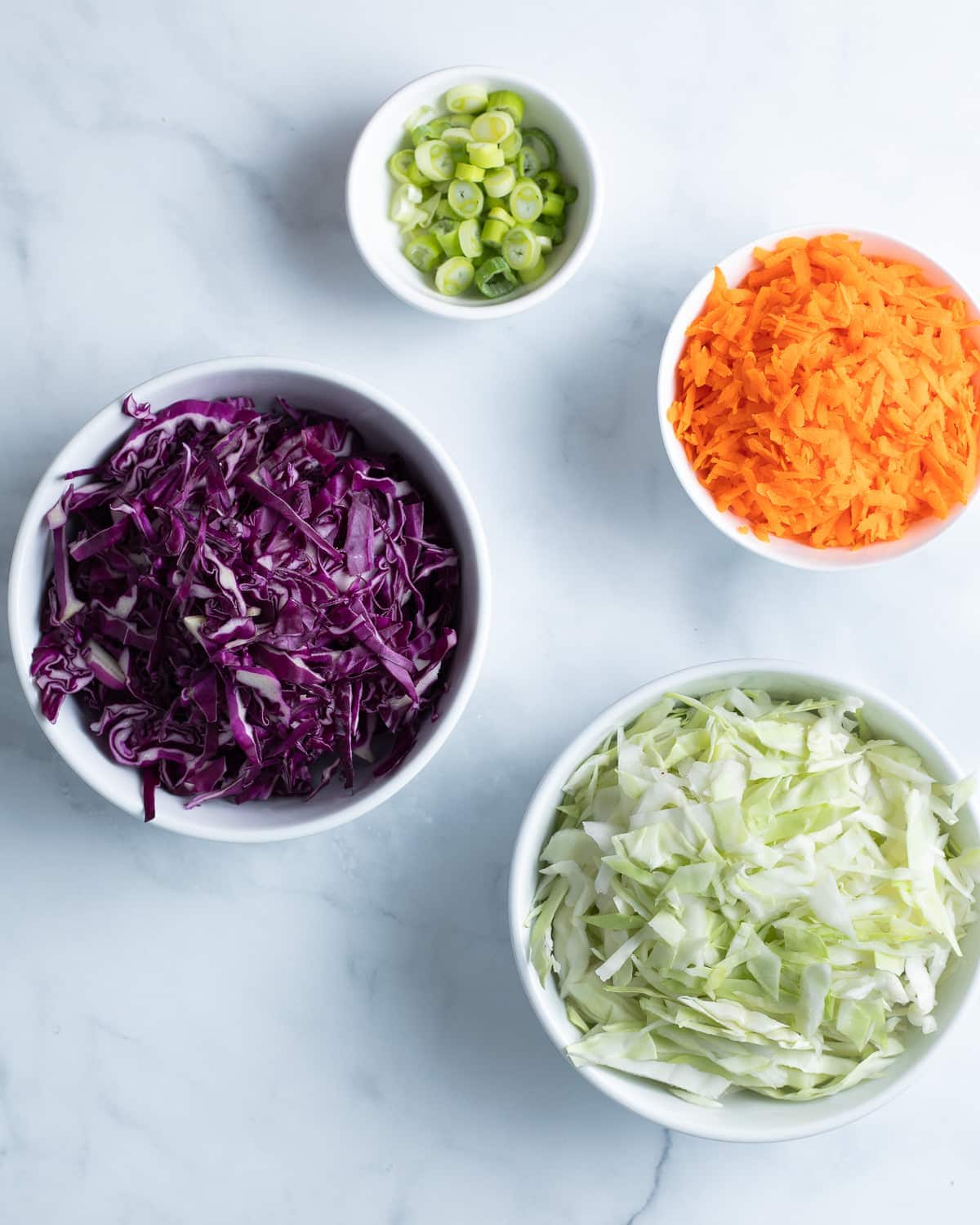 Shredded purple and green cabbage, shredded carrots, and sliced scallions in a bowl.