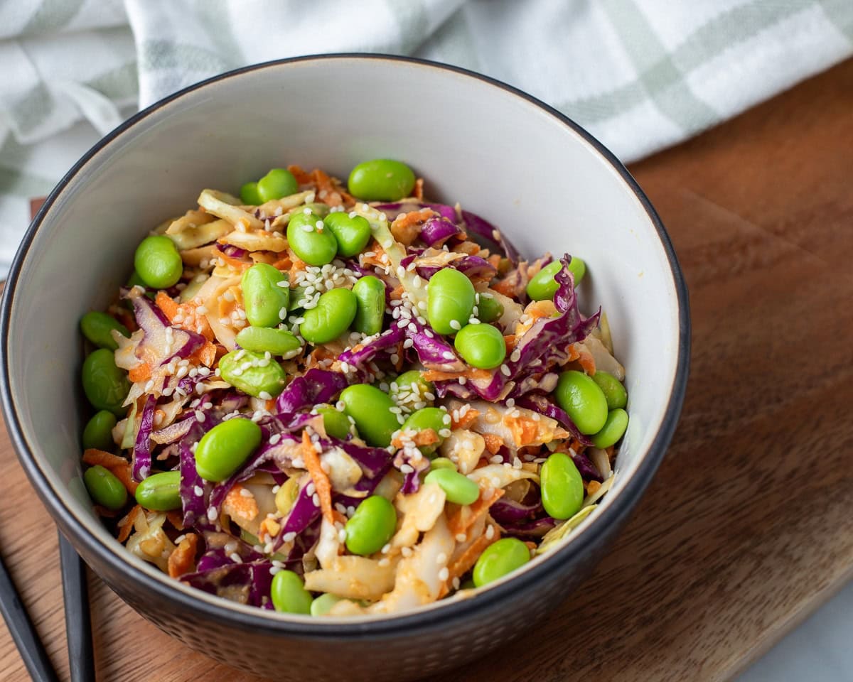 Asian cabbage salad topped with edamame and sesame seeds in a serving bowl.