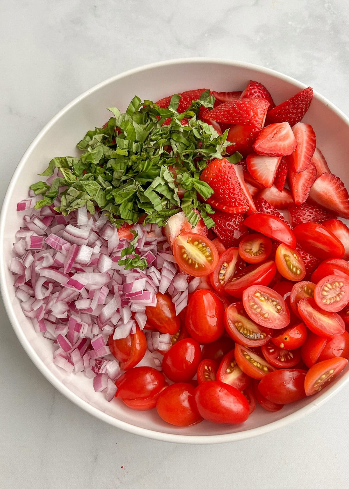 Strawberries, tomatoes, diced red onion, and chopped basil in a large bowl.