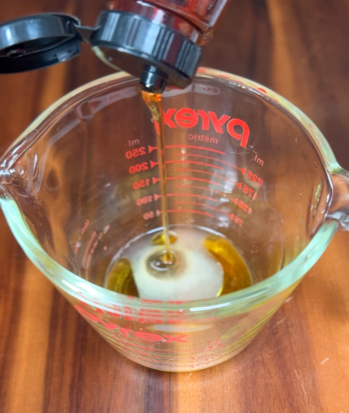 Adding agave syrup to glass measuring cup with lime juice and olive oil. 