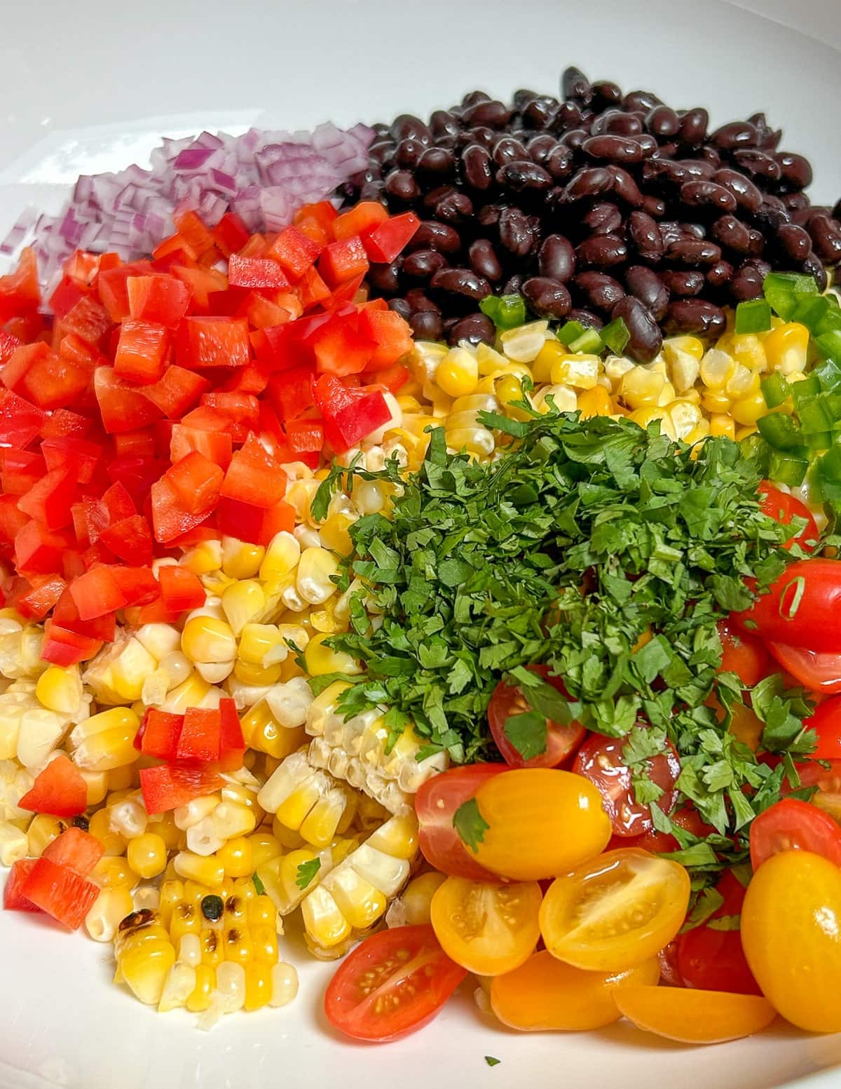Corn, onion, black beans, red pepper, tomatoes, jalapeno, and cherry tomatoes in a bowl.