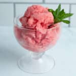 Watermelon ice cream in an ice cream glass served with a sprig of mint.