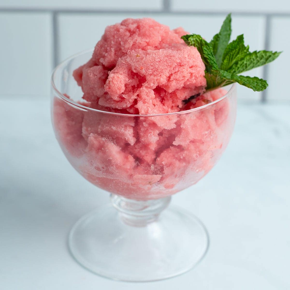 Watermelon ice cream in an ice cream glass served with a sprig of mint.