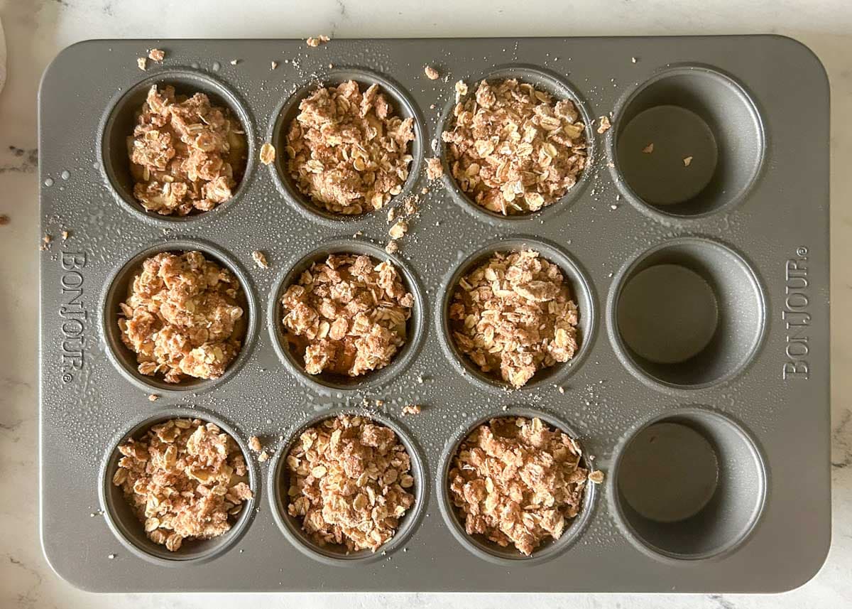Muffin tin filled with batter and topped with streusel topping.