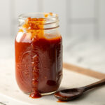Mason jar filled with vegan bbq sauce with some spilling down the edge.