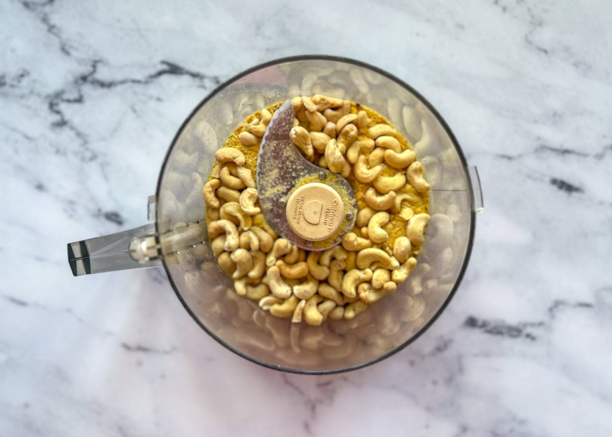 Cashews and seasoning in food processor container.