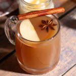 Hot apple cider cocktail in a glass mug served with an apple slice, cinnamon stick, and star anise.