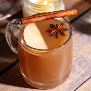 Hot apple cider cocktail in a glass mug served with an apple slice, cinnamon stick, and star anise.