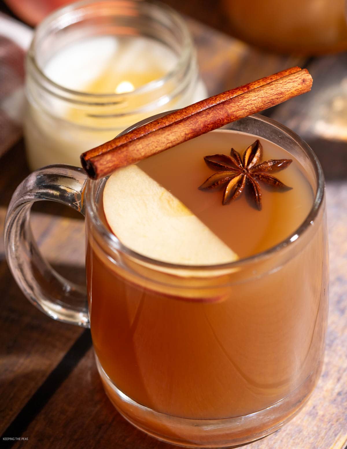 Hot apple cider cocktail in a glass mug garnished with an apple slice, star anise, and a cinnamon stick.