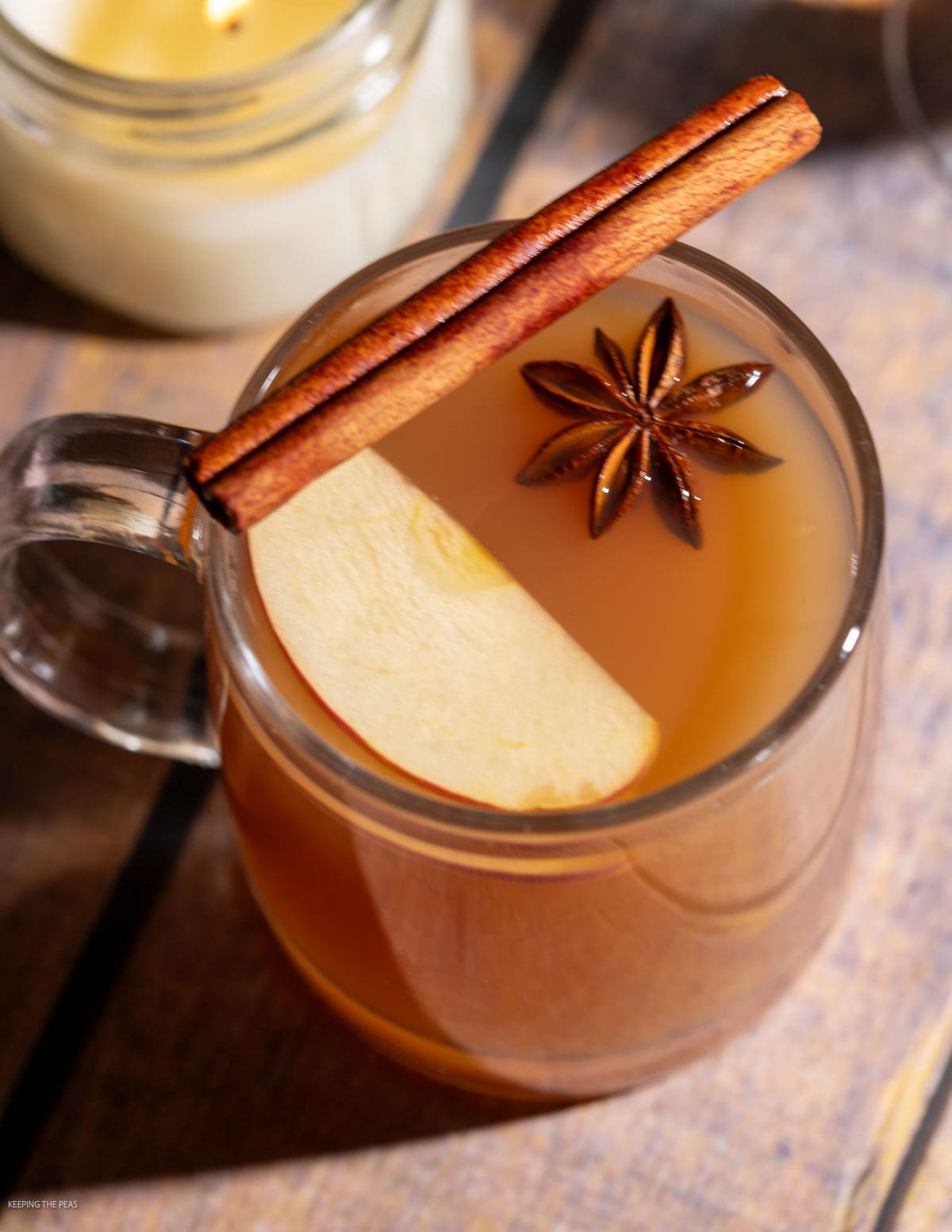 Hot apple cider cocktail served in a glass mug with a slice of apple, star anise, and a cinnamon stick.