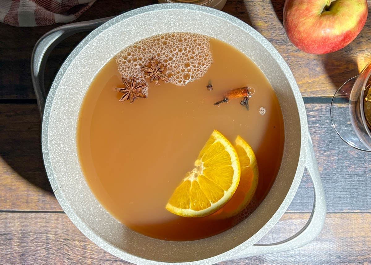 Apple cider with orange slices, star anise, whole cloves, and cinnamon sticks in a pot.