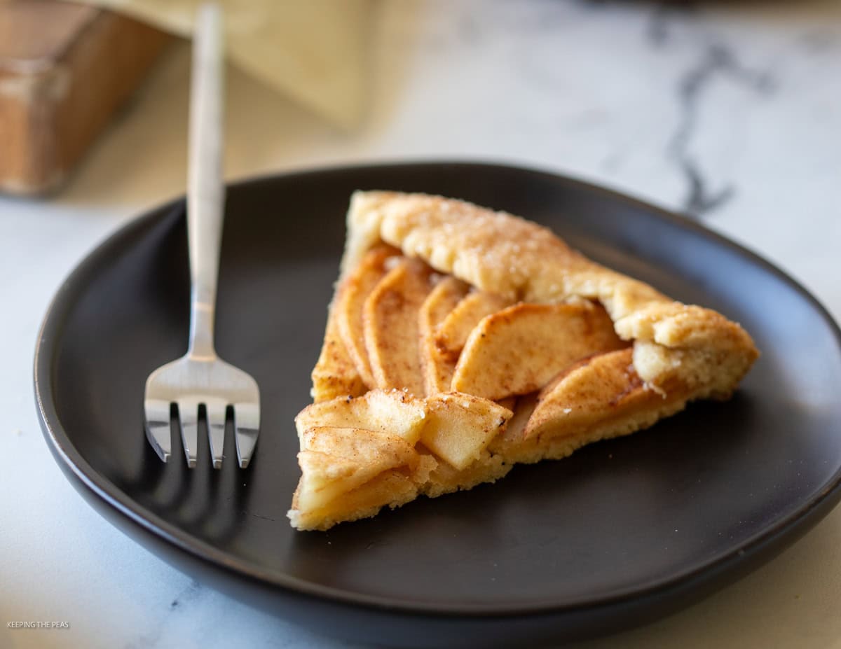 Slice of apple galette on a black plate.