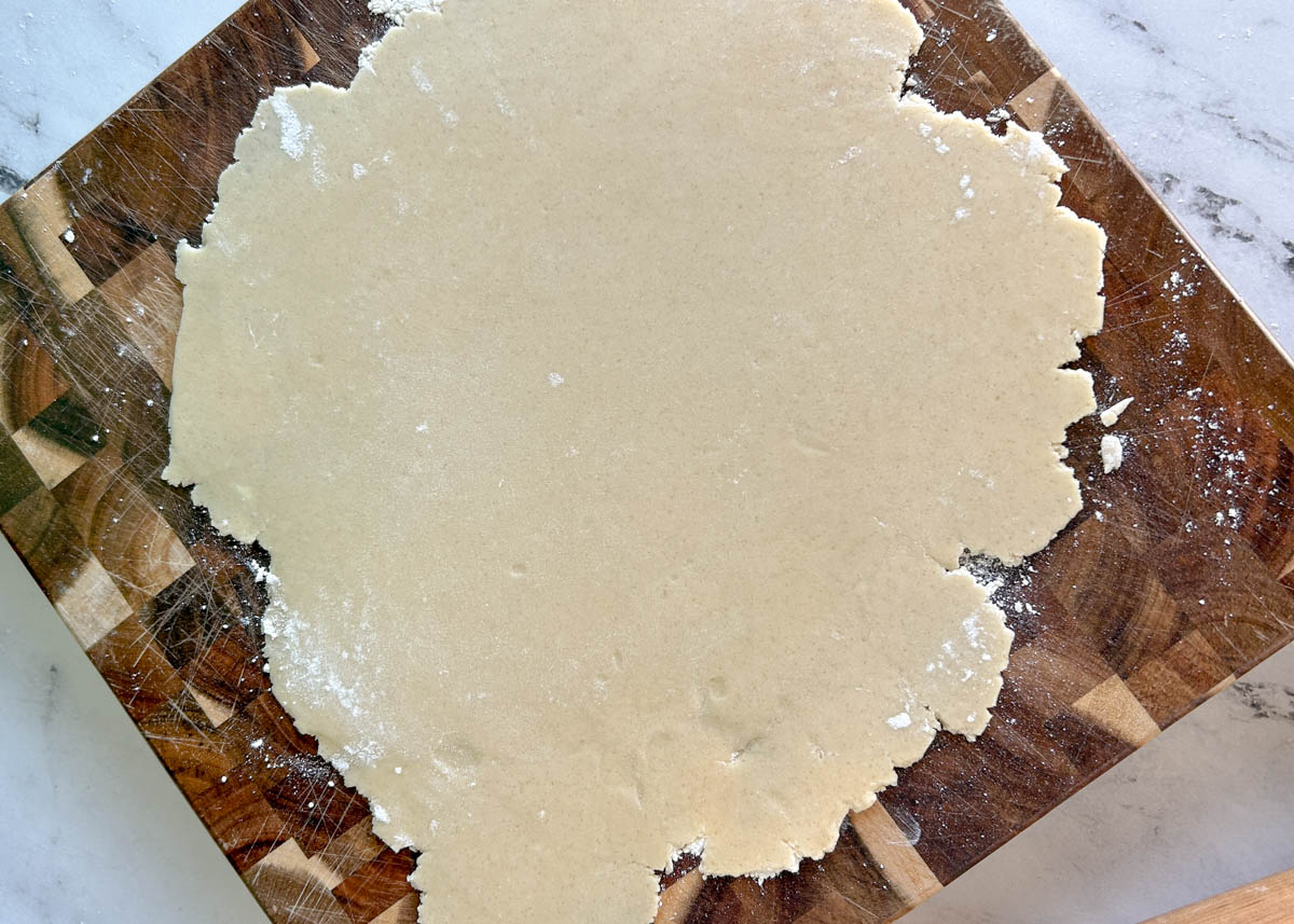 Pie crust rolled into a rustic circle on a wood cutting board.