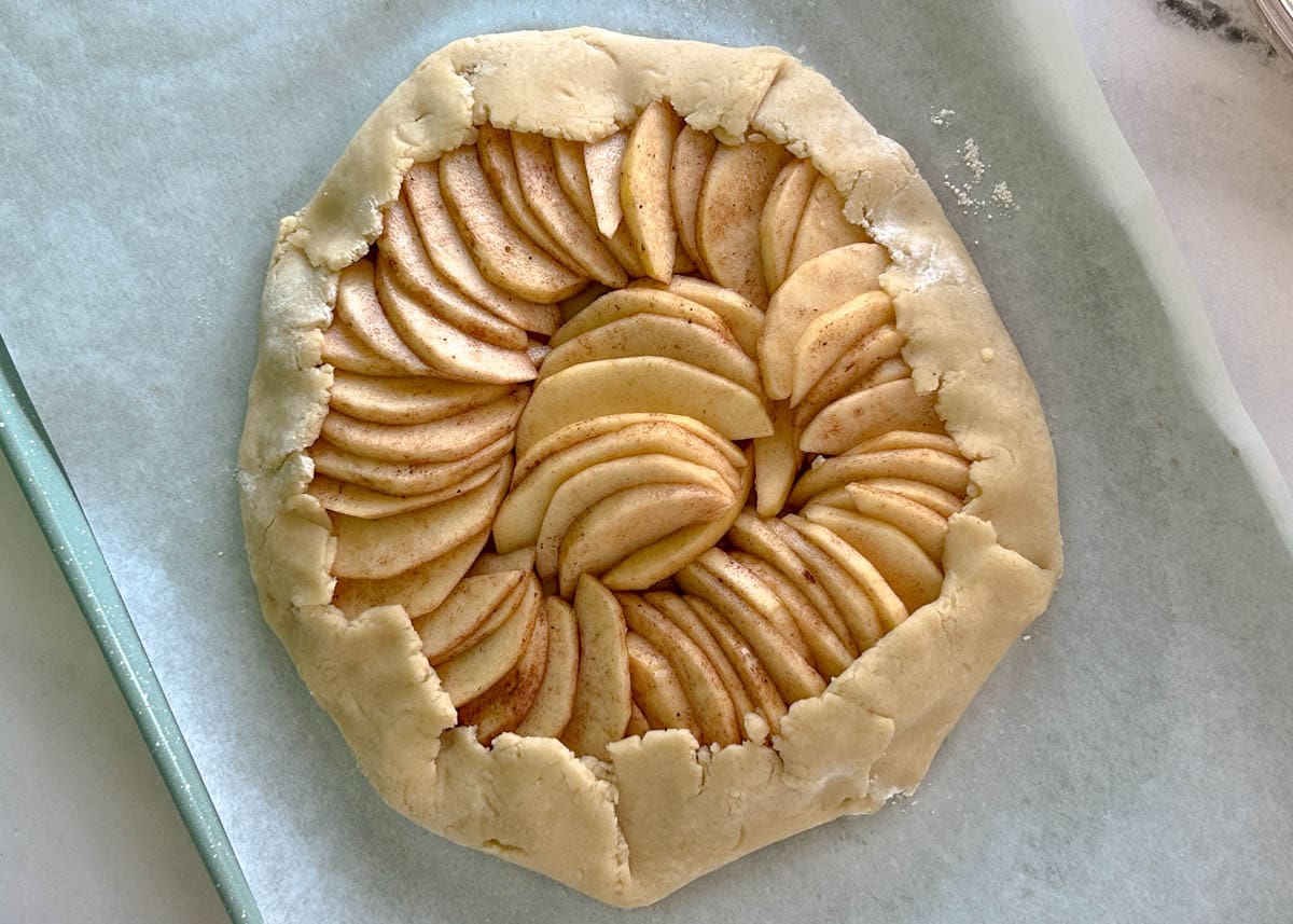 Pre-baked apple galette on baking sheet.