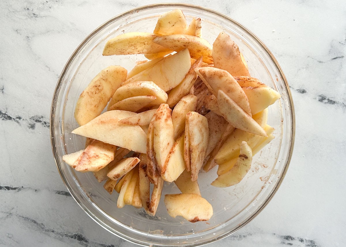 Sliced apples coated in cinnamon in glass bowl.