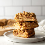 Stack of three apple pie bars on a plate.