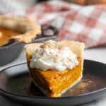Slice of silken tofu pumpkin pie topped with whipped cream on a black plate.