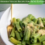 Rigatoni pasta coated in a green sauce in white serving bowl with a gold fork.