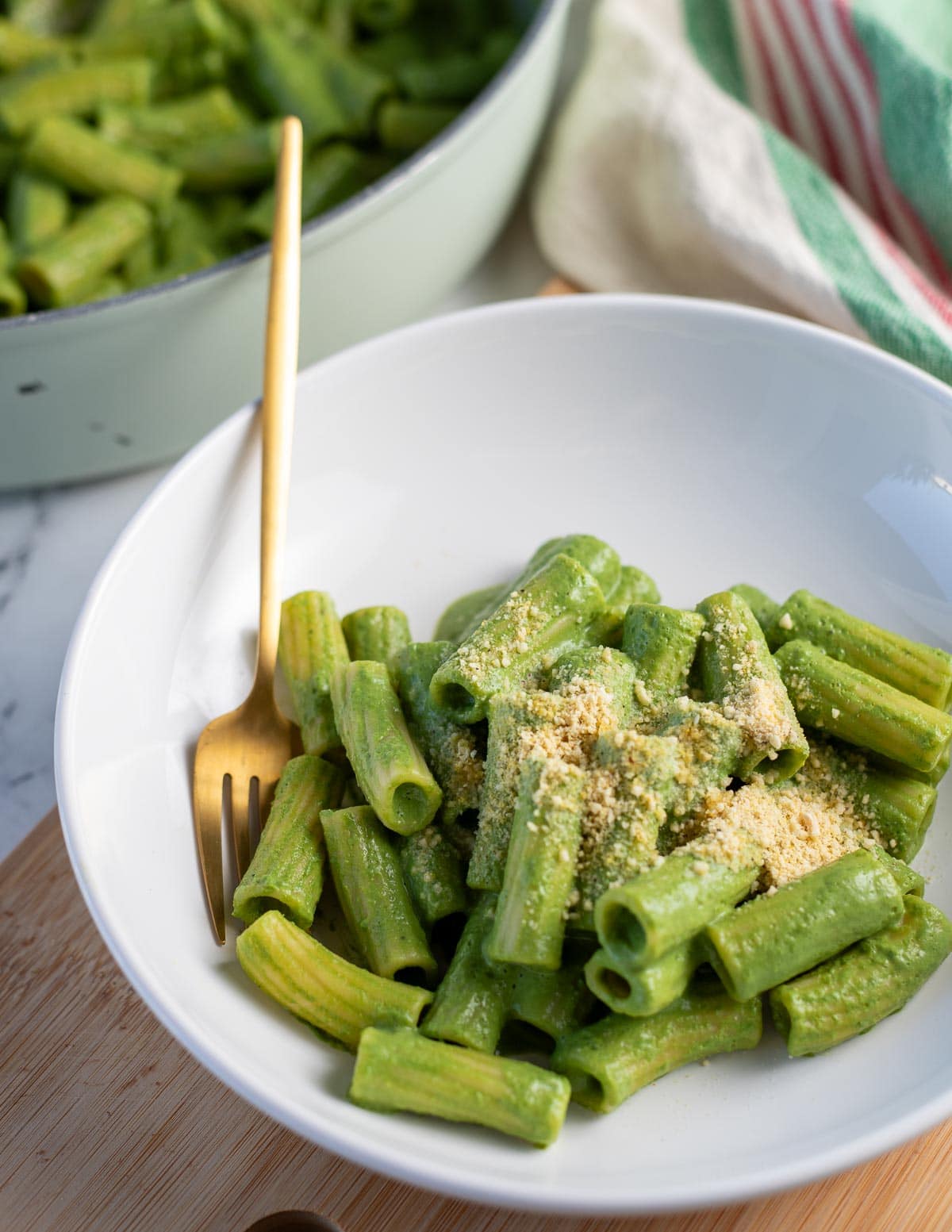Rigatoni pasta coated in a green sauce in white serving bowl with a gold fork.