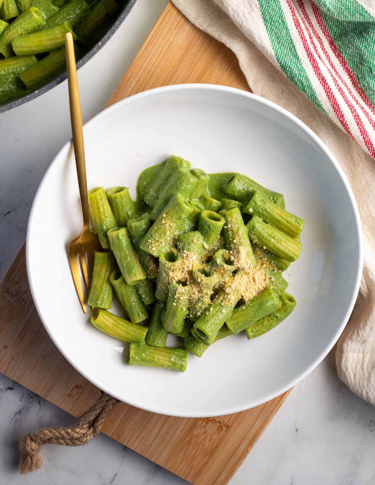 Rigatoni pasta coated in a green sauce in white serving bowl with a gold fork.
