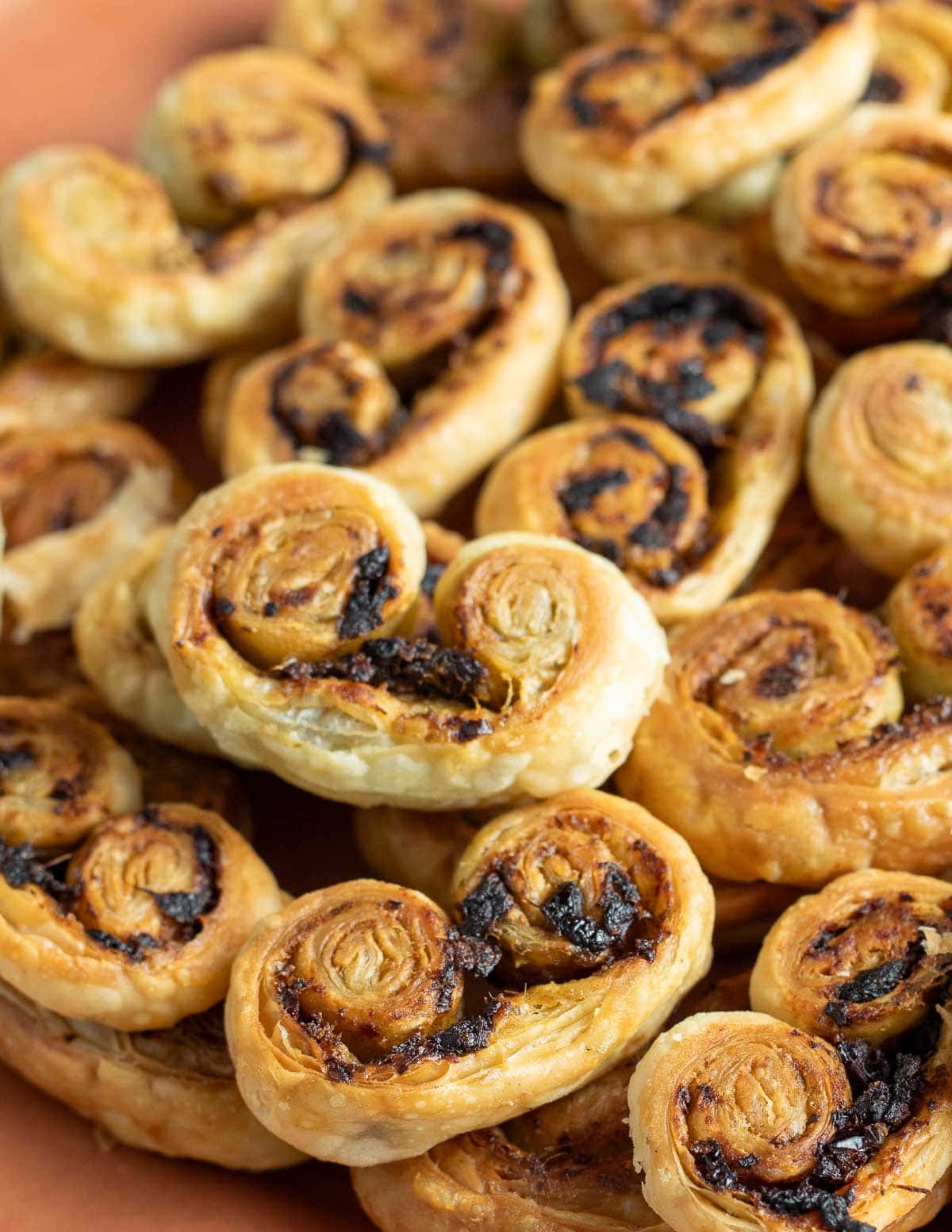 Savory palmiers with pesto and sun-dried tomato on an orange plate.