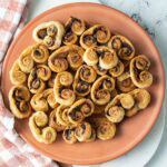 Savory palmiers with sun-dried tomato and pesto on an orange plate.
