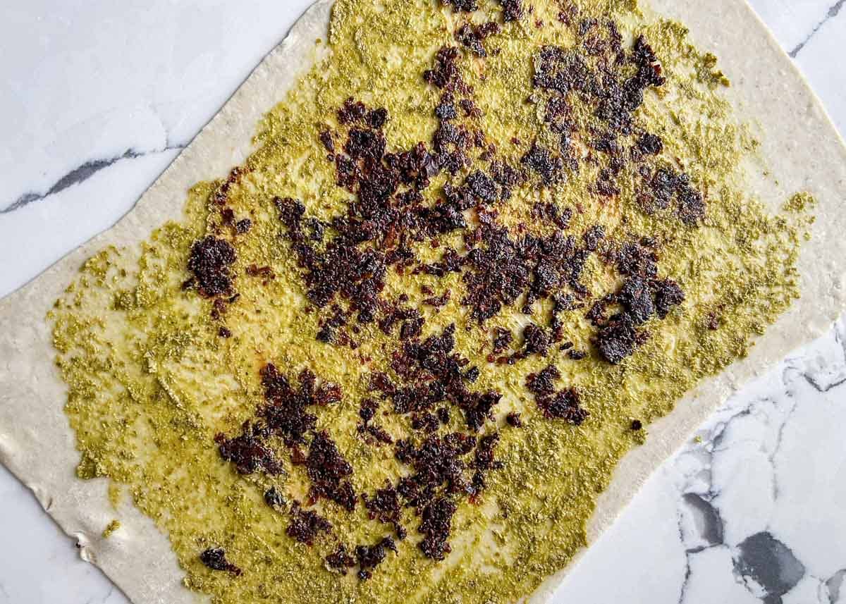 Rolled out puff pastry topped with pesto and sun-dried tomato.