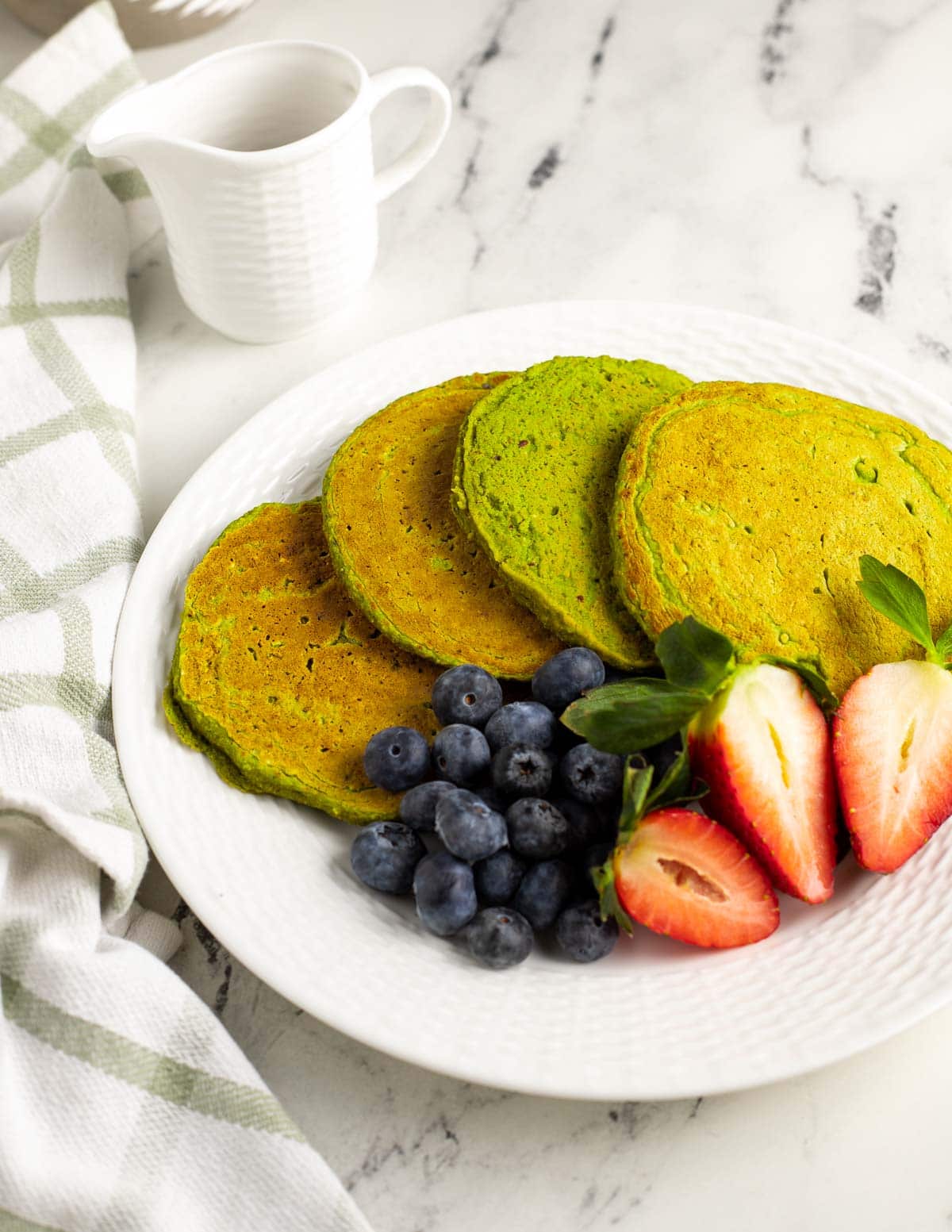Spinach banana pancakes spread on a plate served with blueberries and strawberries.
