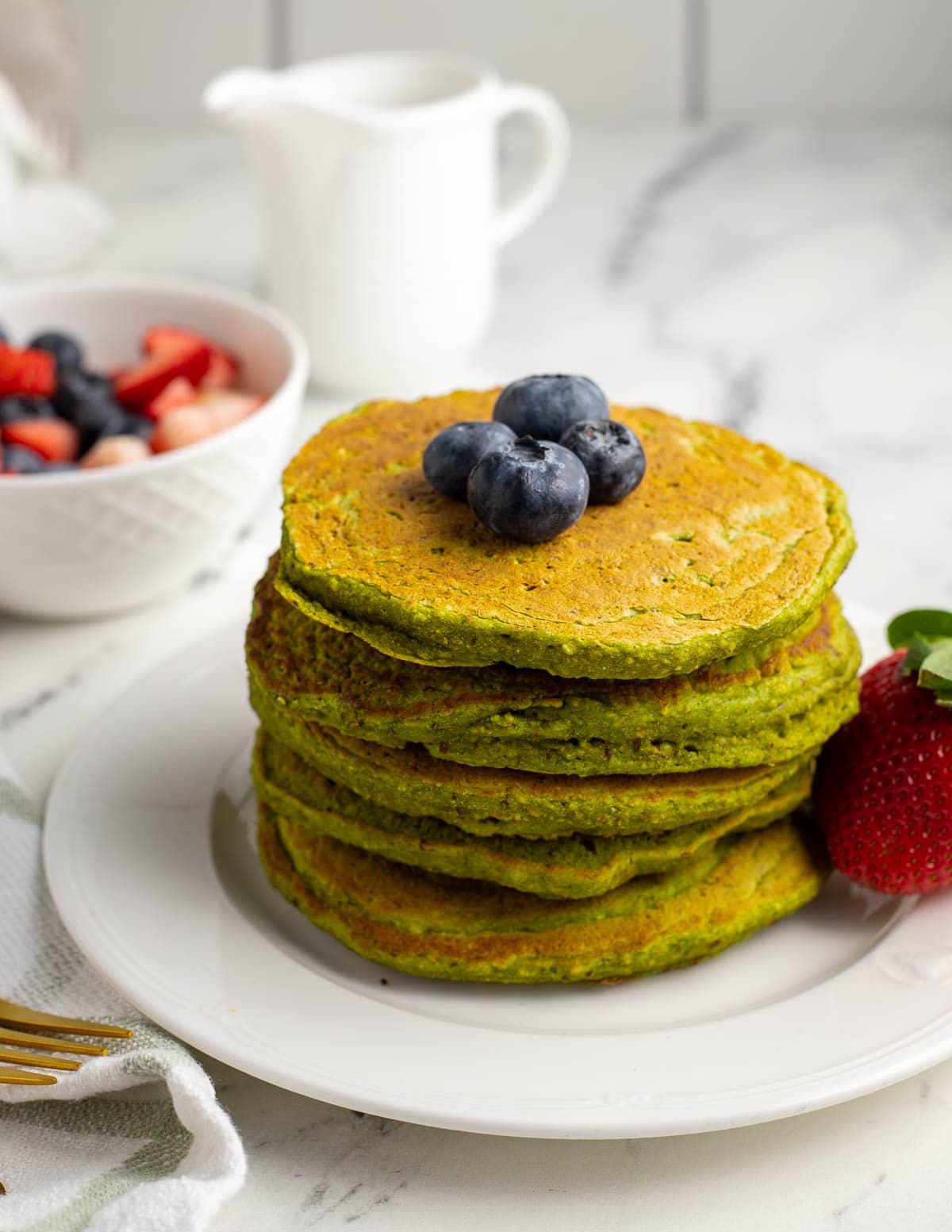 Stack of spinach banana pancakes topped with fresh berries.