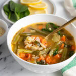 Vegetable orzo soup in a white bowl with a gold spoon.