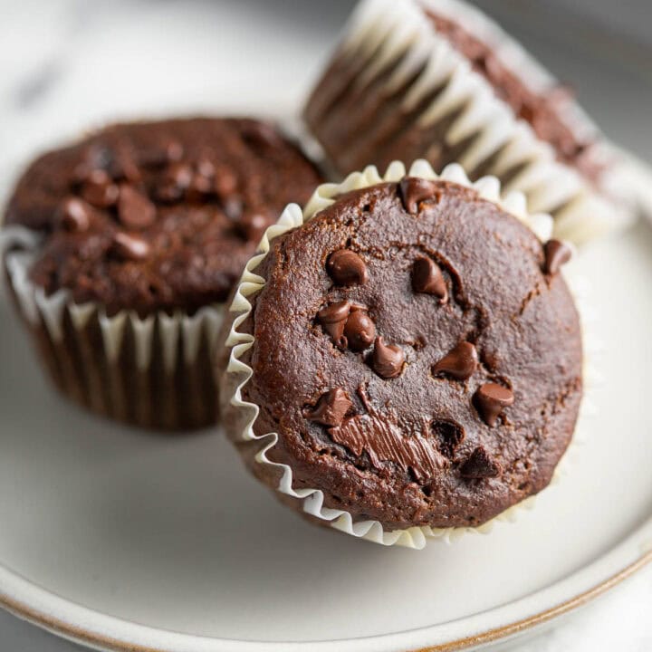 Hidden veggie chocolate muffins topped with mini chocolate chips on a plate.
