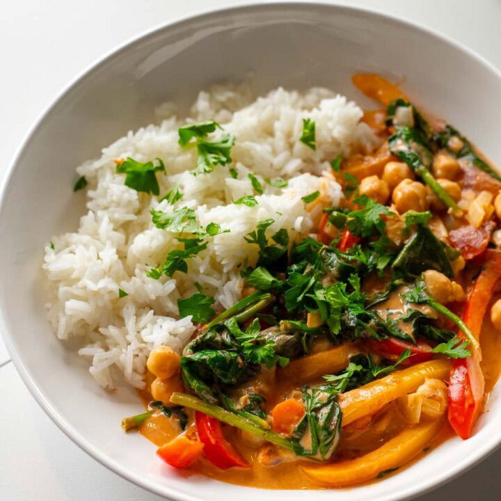 Thai red curry with vegetables and chickpeas served with jasmine rice in a white bowl.